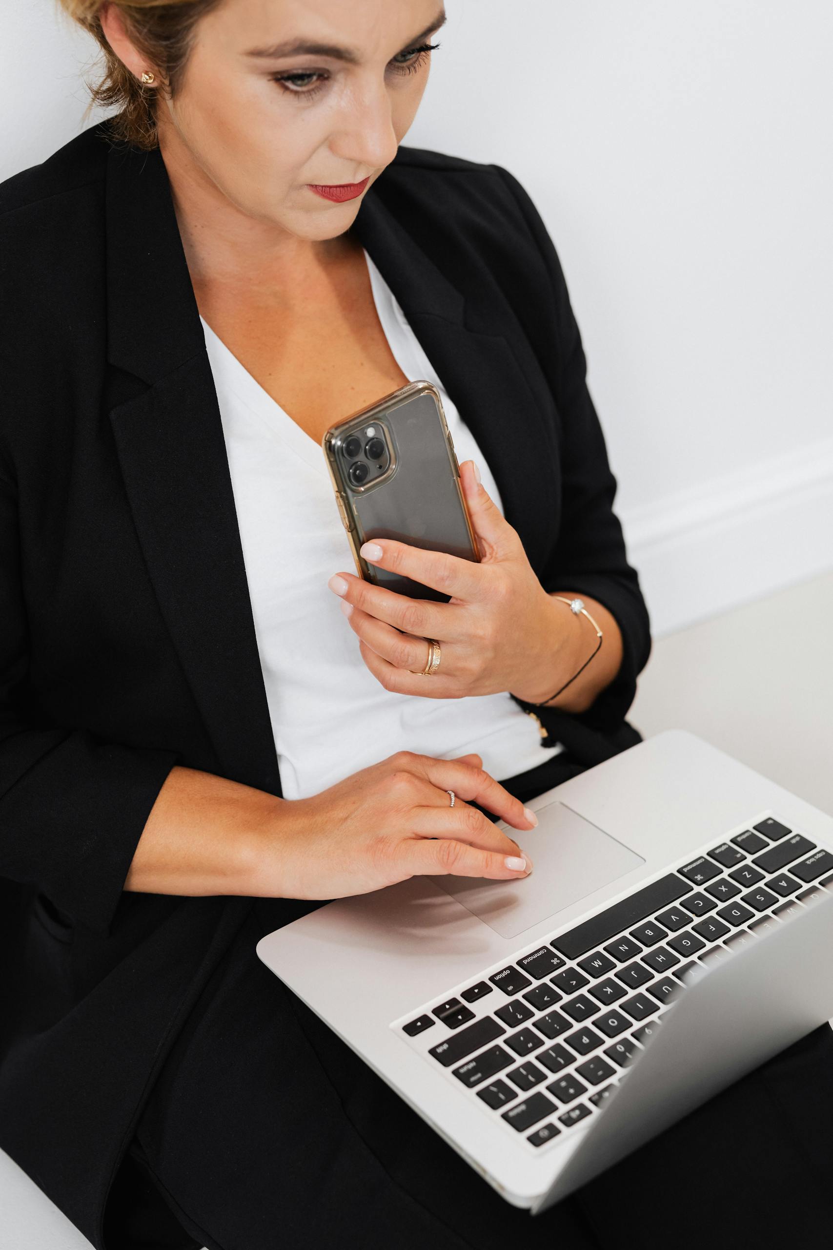 Professional woman multitasking with a laptop and smartphone in an office setting.